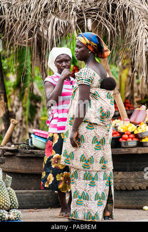 ACCRA, GHANA - MARCH 2, 2012: Unidentified Ghanaian woman with her child on her back at the market in the street in Ghana. People of Ghana suffer of p Stock Photo