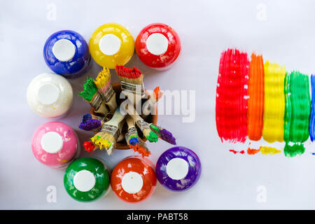 Bottles of colorful paint in the colors of the rainbow arranged in a circle around used paint brushes with vivid bristles viewed from above alongside  Stock Photo