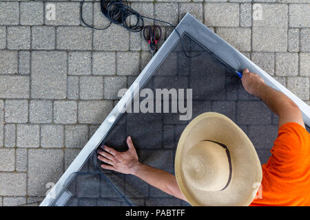 Man wearing hat replacing old material in porch door Stock Photo