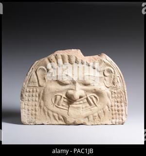Terracotta gorgoneion antefix (roof tile). Culture: Greek. Dimensions: H. 6 3/4 in. (17.1 cm.)  W. 9 5/8 in.  (24.4 cm.). Date: ca. 580-570 B.C..  The frightening features of this Gorgon head, its petrifying eyes and sharp teeth, correspond to its Archaic date and were likely intended to ward off evil. Throughout the following century, the Gorgon tended to lose its more terrifying characteristics, and by the Late Classical period, its features were sweetened. Museum: Metropolitan Museum of Art, New York, USA. Stock Photo