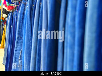 Row of hanged blue jeans in a shop. Clothes store. Shopping in fashion mall. Garments on hangers. Stock Photo
