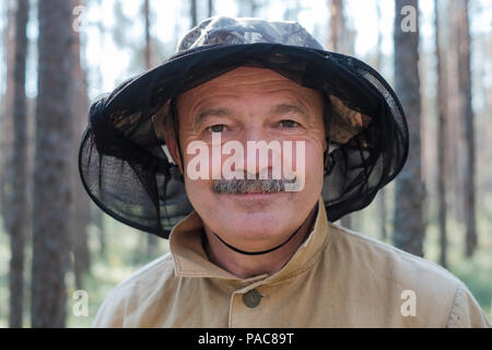 Closeup portrait of a senior man in special hat against mosquito standing in forest. Stock Photo