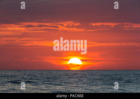 Sun going down parially behind clouds in orange sky over water in the the Gulf of Mexico Stock Photo