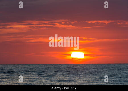 Sun going down parially behind clouds in orange sky over water in the the Gulf of Mexico Stock Photo