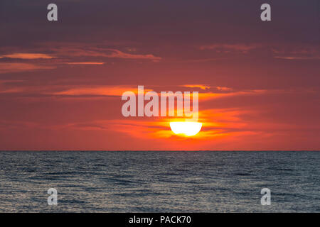 Sun going down parially behind clouds in orange sky over water in the the Gulf of Mexico Stock Photo