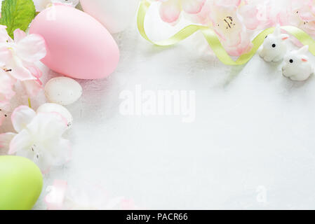 Beautiful delicate Easter frame with pink cherry flowers, multicolored Easter eggs and  Easter bunny on the stone background, with copy-space Stock Photo