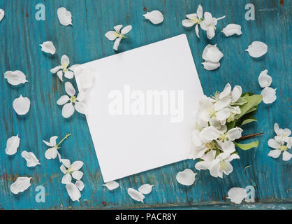 Scrapbook page of wedding or family photo album with copy-space, frame with white paper card, apple flowers and green leaves on blue wooden background Stock Photo