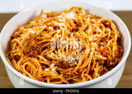 Spaghetti Bolognese in a deep white bowl on the wooden kitchen table waiting to be eaten Stock Photo
