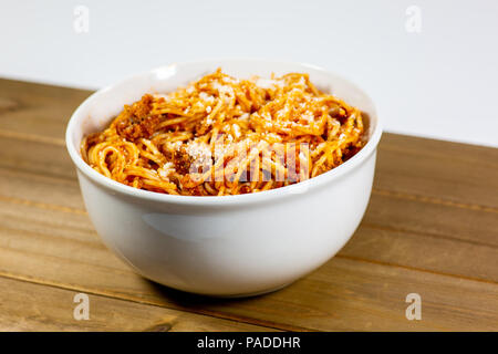 Spaghetti Bolognese in a deep white bowl on the wooden kitchen table waiting to be eaten Stock Photo
