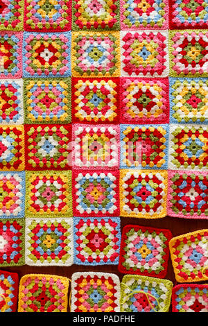 Brightly coloured granny square woollen baby blanket, traditional hand made crochet home handicraft, squares being stitched together Stock Photo