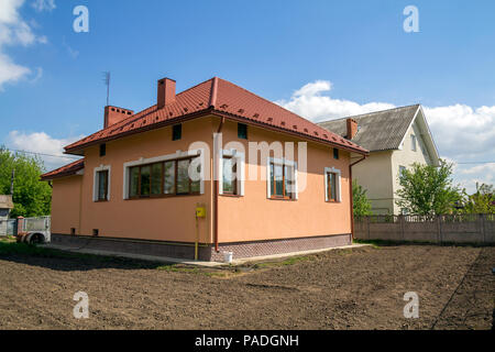 New built one-store cottage house with red tiling roof, plastic windows, plastered walls and high chimneys on fenced land plot in quiet neighborhood.  Stock Photo