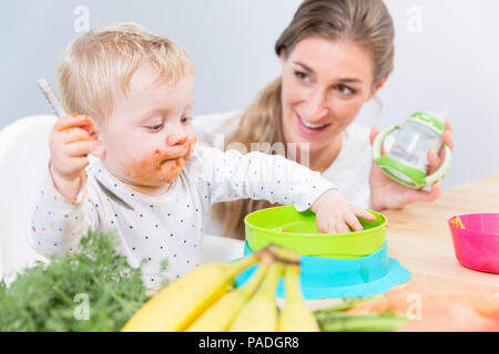 Portrait of a cute baby sitting on high chair while eating solid food Stock Photo