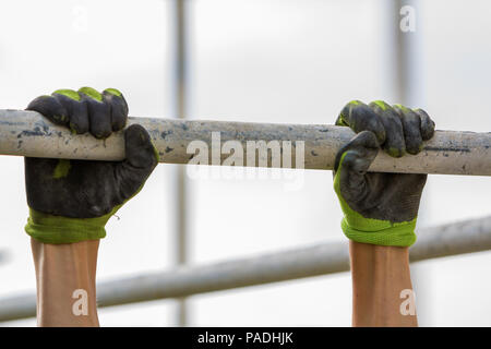 Close-up of muscular worker hands hanging on scaffold metal pipe on white house wall with polyurethane foam sheet background. Modern technology, renov Stock Photo