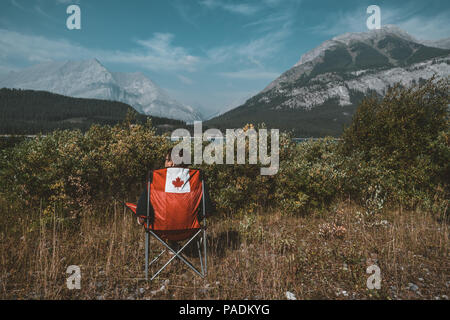 Bright red chairs with canada logo overlooking grass and mountains with lake in Lower Kananaskis Lake, Canada Stock Photo