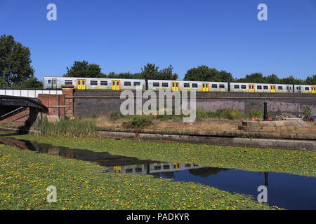 A Mersey rail train travelling from Liverpool to Southport crosses the Leeds and Liverpool canal near the Caroline Street footbridge in Bootle. Stock Photo