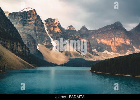 Sunrise with turquoise waters of the Moraine lake with sin lit rocky mountains in Banff National Park of Canada in Valley of the ten peaks. Stock Photo