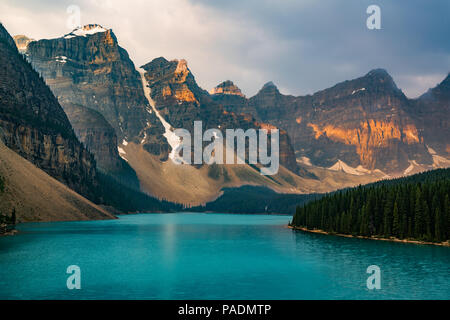 Sunrise with turquoise waters of the Moraine lake with sin lit rocky mountains in Banff National Park of Canada in Valley of the ten peaks. Stock Photo