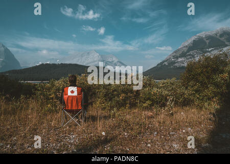 Bright red chairs with canada logo overlooking grass and mountains with lake in Lower Kananaskis Lake, Canada Stock Photo