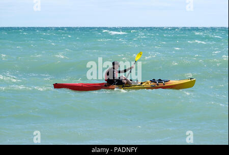 Man wearing life jacket paddling his Kayak in choppy seas off the coast of East Preston, West Sussex, UK. Direction East to West. Stock Photo