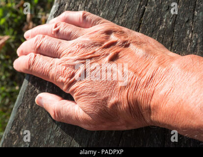 Old man's hand resting on wood lit by sunlight Stock Photo