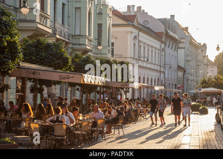 SZEGED, HUNGARY - JULY 2, 2018: Young people walking on a pedestrian street of Szeged, Southern Hungary, with other people sitting on tables in cafes  Stock Photo