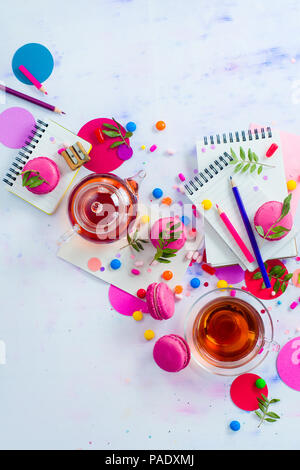 Glass teapot with candies and confetti on a light background with copy space. Pink and purple palette still life. Vibrant tea party drinks flat lay. Stock Photo