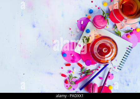 Glass teapot header with candies and confetti on a light background with copy space. Pink and purple palette still life. Vibrant tea party drinks flat Stock Photo