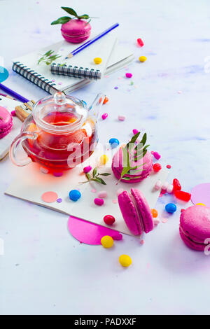 Transparent teapot, candies and confetti from above. Planning and creative work still life with copy space. Drinking tea and working concept. Stock Photo