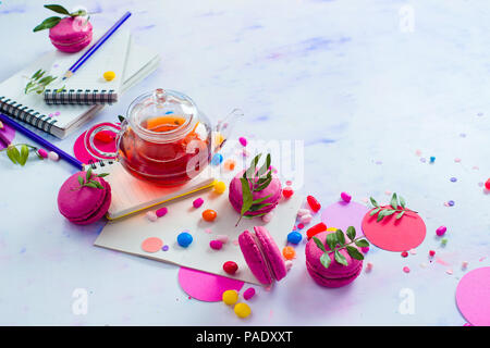 Glass teapot header with candies and confetti on a light background with copy space. Pink and purple palette still life. Vibrant tea party drinks concept Stock Photo
