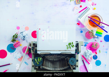 Writer workplace with tea cup, teapot, notepads with blank pages, candies and confetti from above. Planning and creative work still life with copy space. Drinking tea and working concept. Stock Photo