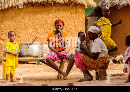 ACCRA, GHANA - MARCH 6, 2012: Unidentified Ghanaian women and their children on a bench near their house in the street in Ghana. Children of Ghana suf Stock Photo