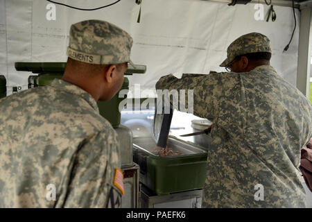 Ssg. Raymond King (right), pours the beef from the T-ration as the Cooks from the Wiesbaden Strong Teams Cafe Dining Facility (DFAC) brought a Mobile Kitchen Trailer (MKT) out to the Wackernheim Regional Range Facility on 30 March 2016 to feed the U.S. Army Europe Soldiers. The three cooks, (NCO Ssg. Raymond King, and Spc. Michelle Santiago-Lopez, and Spc. Kallan Clements) and one grill mechanic (Spc. Luke Wilson), set up the MKT, prepared the meals, fed the Soldiers, cleaned the MKT, and broke down the trailer to be used next time. After a long period of not being used, this is the first time Stock Photo