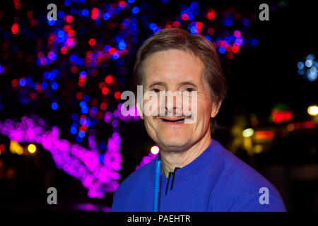 A happy, older, toothless man with Downs Syndrome smiles for the camera.  He is standing in front of bokeh from Christmas lights.  He has two markers  Stock Photo