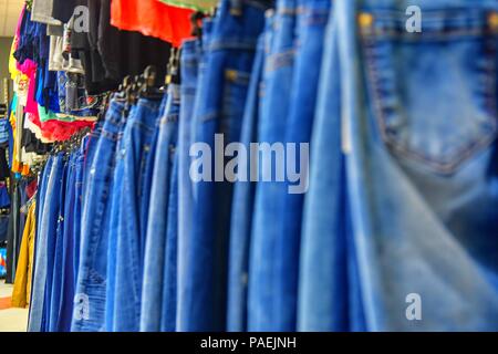 Row of hanged blue jeans in a shop. Clothes store. Shopping in fashion mall. Garments on hangers. Clothes on the store shelves. Blurred view, defocude Stock Photo