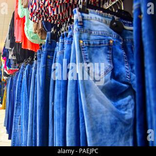 Row of hanged blue jeans in a shop. Clothes store. Shopping in fashion mall. Garments on hangers. Clothes on the store shelves. Blurred view, defocude Stock Photo