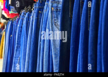 Row of hanged blue jeans in a shop. Clothes store. Shopping in fashion mall. Garments on hangers. Blurred view, defocuded. Stock Photo