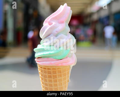 Melting Pastel Color Soft Serve Ice Cream Cone with Blurred Shopping Arcade in Background Stock Photo
