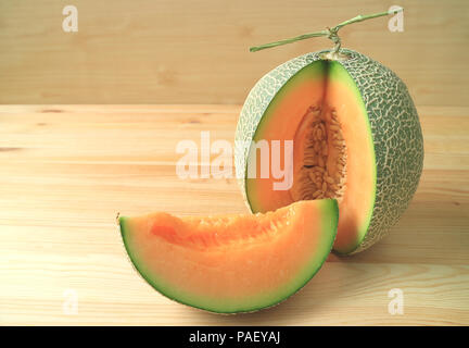 Bright orange color juicy ripe cantaloupe melon sliced from whole fruit isolated on wooden table Stock Photo