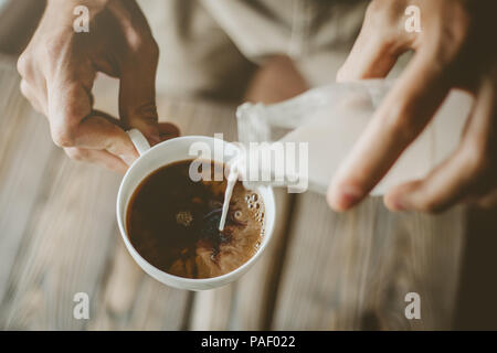 Young man preparing coffee with milk. Pouring milk in coffee. Closeup Stock Photo