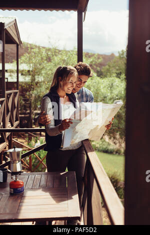 Couple standing in their hotel room balcony and looking at map. Man and woman reading map for finding nearest tourist attraction. Stock Photo