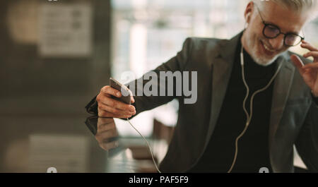 Mature businessman sitting at cafe counter with smart phone in hand. Focus on male hand holding mobile phone. Stock Photo