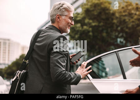 Happy mature commuter getting into a taxi. Businessman entering a taxi with driver opening door. Stock Photo