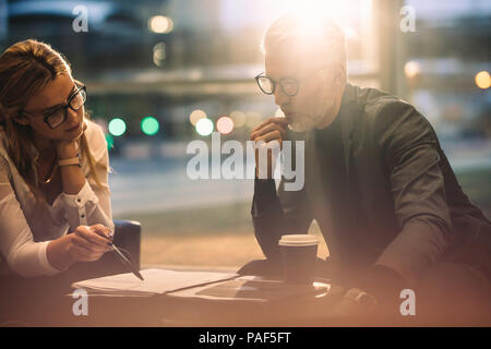 Two business people discussing over some paperwork while in office lobby. Business people working together in office. Stock Photo