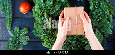 fruits, box with a gift in gray paper in the hands of a woman and a green Christmas tree on a blue wooden background Stock Photo
