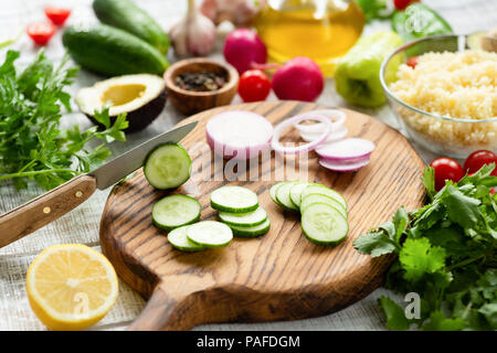 Cooking process. Fresh vegetables on cutting board. Tomato, purple onion, cucumber, lemon, parsley, couscous and avocado ready for salad Stock Photo