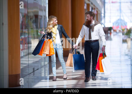 Happy beautiful young couple with shopping bags walking holding hands in mall Stock Photo