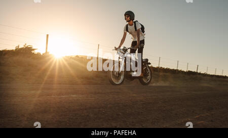 Biker standing on his bike while driving through country road. Young man riding off-road on vintage bike. Stock Photo