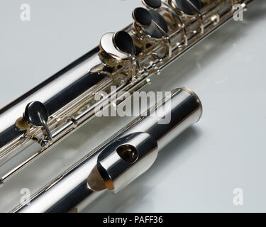 Details of a silver bass flute lying on a white reflective surface Stock Photo