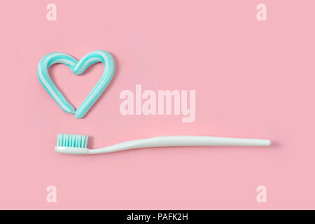 Toothbrushes and turquoise color toothpaste in shape of heart on pink background. Dental and healthcare concept. Stock Photo