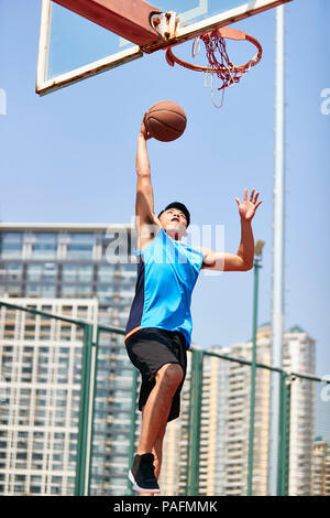 young asian adult dunking basketball on outdoor court. Stock Photo